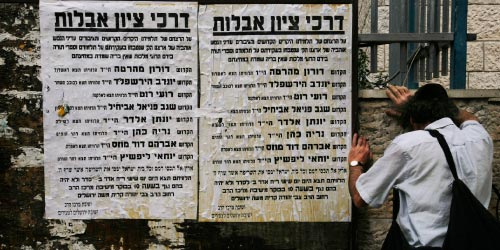 يهودي يصلي قرب ملصق يحمل أسماء قتلى العملية الفدائية في القدس الغربية (كيفين فراير - أ ب)