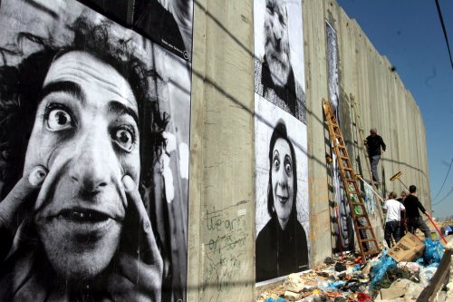 أعضاء في مشروع «وجهاً لوجه» الفنّي الداعي للسلام يضعون ملصقات على جدار الفصل في بيت لحم أمس (إي بي أي)