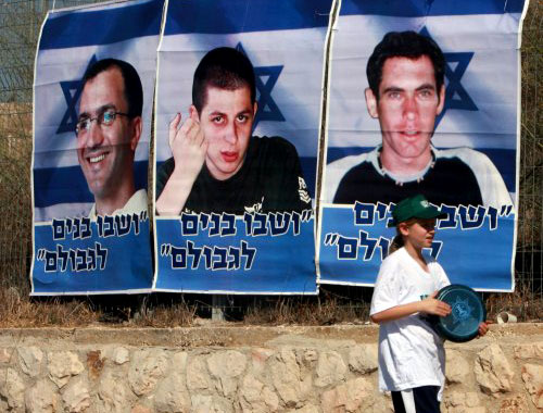 إسرائيلية تمر أمام ملصق للجنديين الإسرائيليين الأسيرين في لبنان يتوسطهما الجندي الأسير في قطاع غزة (إي بي إ