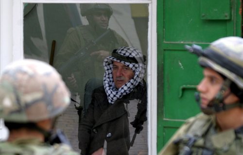 فلسطيني يراقب جنديّين إسرائيليّين يرافقان مستوطنين في الخليل أمس (إي بي أي)