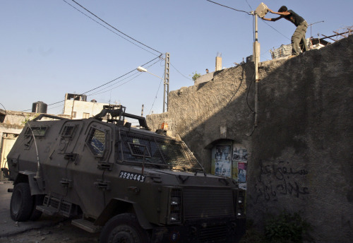 فلسطيني يرمي حجراً على آلية عسكرية إسرائيلية قرب جنين أمس (محمد بلاص - أ ب)