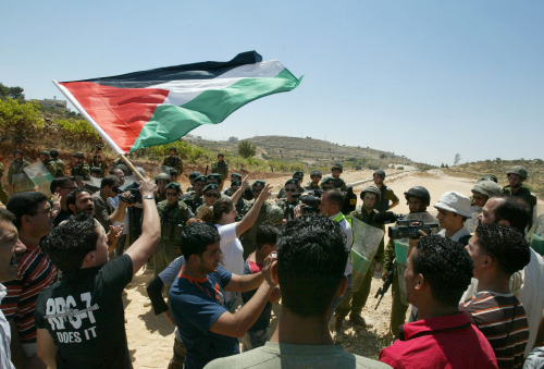 ناشطو سلام يتظاهرون ضدّ الجدار العازل وأمامهم جنود اسرائيليون في الضفّة الغربية أمس (موسى الساهر