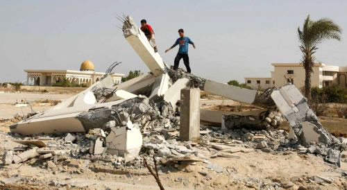 فلسطينيان على انقاض جزء من مطار غزة الدولي بعد استهدافه بغارات اسرائيلية أمس (إبراهيم ابو مصطفى - رويترز)