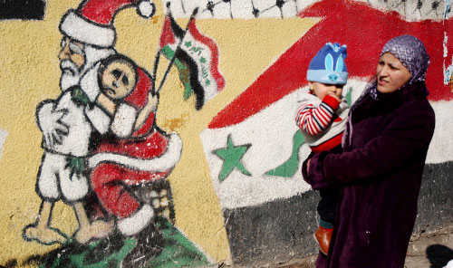 فلسطينية تمرّ أمام جداريات تجسّد الأجواء الميلاديّة في رام الله أمس (مجدي محمد ـ أ ب)