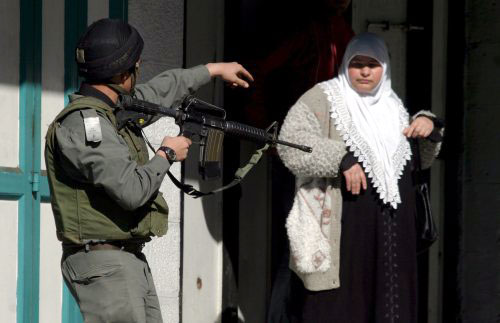 جندي إسرائيلي يوجّه بندقيّته باتّجاه فلسطينيّة في الخليل أمس (عبد الحفيظ هشملون ـ إي بي أي)