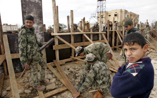 فتى فلسطيني قرب عناصر أمن مصريين يعيدون بناء الجدار الحدودي في رفح (محمد سالم ـ رويترز)