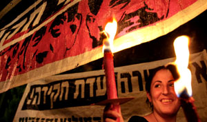 إسرائيلية تحمل مشعلا تحت ملصق لبيرتس خلال تظاهرة في القدس المحتلة ليل الخميس (أ ف ب)