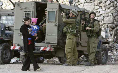 فلسطينية تحمل طفلتها وتمر أمام دورية إسرائيلية في بيت لحم أمس (رويترز)