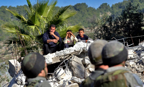 فلسطينيون يجلسون على أنقاض منزلهم في الضفة الغربية أمام أنظار جنود إسرائيليين أمس (أ ف ب)