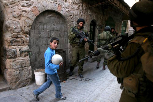 طفل فلسطيني يمر أمام جنود إسرائيليين في مدينة الخليل القديمة أمس (إي بي إي)