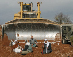مزارعون فلسطينيّون يجلسون في طريق جرافة إسرائيليّة أثناء تشييد جزء من جدار الفصل أمس (أ ف ب)