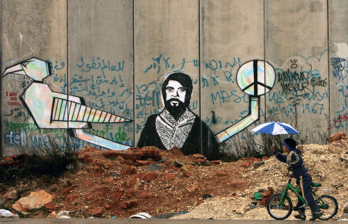 فتى فلسطيني ينظر إلى جداريّة على جدار الفصل عند قلنديا قرب رام الله أوّل من أمس (أ ب)