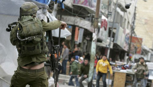 جندي إسرائيلي يرشق قنبلة أثناء احتجاج في الخليل أمس (رويترز)