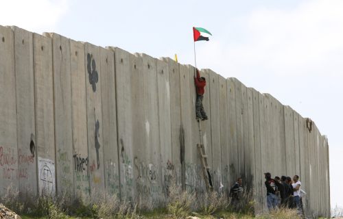 فلسطيني يرفع علم بلاده أثناء تسلّقه جدار الفصل عند نقطة قلنديا قرب رام الله أمس (رويترز)