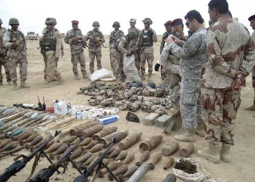 جنود أميركيّون وعراقيّون يعرضون أسلحة وذخائر مصادرة في المحموديّة جنوب بغداد أمس (رويترز)