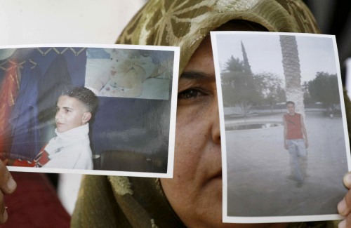 فلسطينيّة ترفع صورتين لابنها المعتقل في سجون الاحتلال خلال احتجاج في الخليل أمس (نايف هشلمون - رويترز)