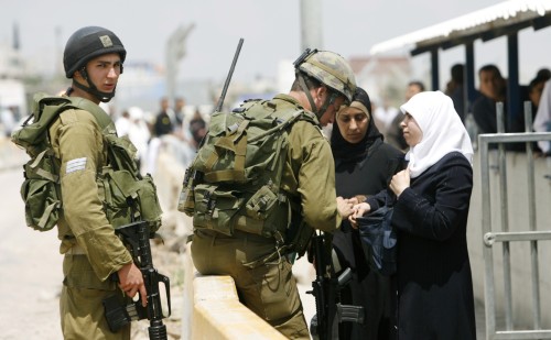 جنديّ للاحتلال يفتّش فلسطينيّتين عند نقطة حوارة الأمنيّة في نابلس أمس (لؤي أبو هيكل - رويترز)