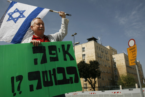 إسرائيلي يرفع عبارة «أين الحياء؟» أمام مكتب أولمرت في القدس المحتلّة أمس (كيفين فريير - أ ب)