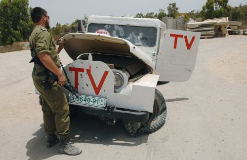 جندي اسرائيلي أمام سيارة تحمل شارة تلفزيون في كيسوفيم جنوبي غزّة أمس (عمير كوهين - رويترز)