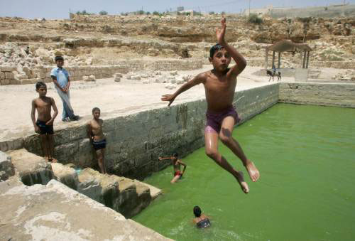 طفل فلسطيني يقفز في بركة ماء في الخليل (نايف هاشلمون - رويترز)
