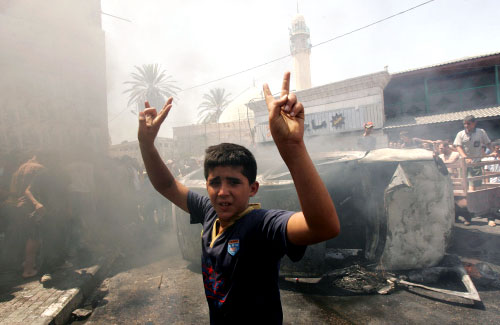 فتى فلسطيني ينظر إلى بقايا سيارة محترقة قادها جندي إسرائيلي في جنين أمس (صايف دحلح - أ ف ب)