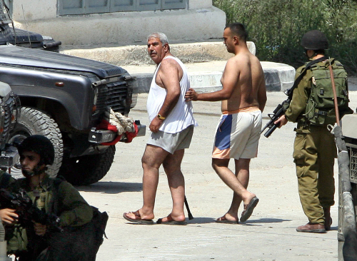 جندي اسرائيلي يحتجز فلسطينيين بعد تعريتهما في قلقيلية أول من أمس (جعفر أشتياه - أ ف ب)