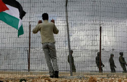فلسطيني يتمسّك بسياج يفصله عن دوريّة إسرائيليّة في بلدة بلعين في الضفّة الغربيّة أمس (بيتر أندروز ـ رويترز)