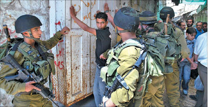 جنود اسرائيليون يفتشون فلسطينيا في الخليل في الضفة الغربية أمس