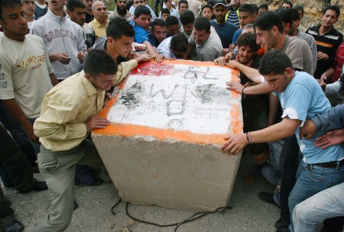 فلسطينيون يزيلون حجراً ضخماً خلال تظاهرة ضدّ جدار الفصل قرب رام الله أمس (عمار عوض - رويترز)