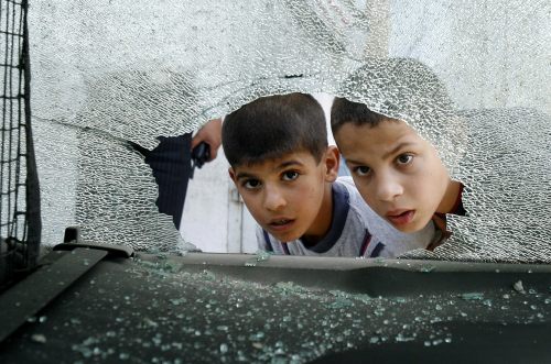 طفلان فلسطينيان  ينظران من خلف زجاج احدى السيارات المحطمة بعد غارات أمس في غزة  (سهيب سالم - رويترز)