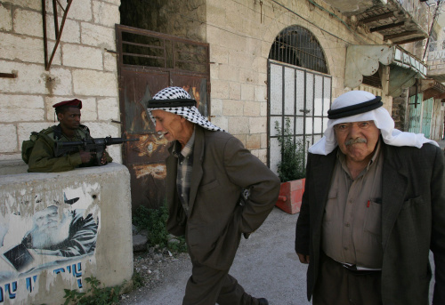 فلسطينيّان يمرّان أمام جندي اسرائيلي في الخليل أمس (حازم بادر - أ ف ب)