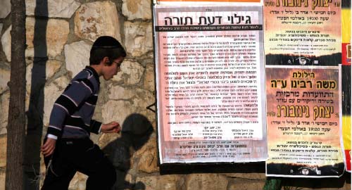 فتى إسرائيلي يمرّ بجانب ملصقات تدعو إلى «الانتقام» لمقتل طلّاب المدرسة اليهوديّة (مناحيم كاهانا ـ أ ف ب)