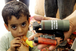 طفل عراقي يضع لعبة على شكل مسدّس في فمه ووالده يعرض مخلّفات للجيش (كريم كاظم ـــ أ ب)