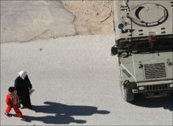 فلسطينية وابنتها تمران قرب آلية عسكرية اسرائيلية خلال المواجهات في نابلس أمس (رويترز)