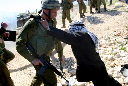 عجوز فلسطيني يواجه جنديّاً إسرائيليّاً خلال ذكرى «يوم الأرض» في بلعين قرب رام الله أمس  (أ ف ب)