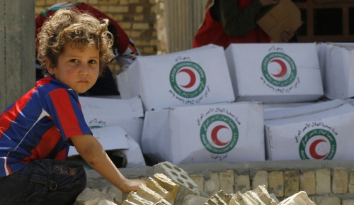 فتى عراقي قرب صناديق مساعدات غذائيّة وزّعتها منظّمة «الهلال الأحمر» في بغداد أمس (رويترز)