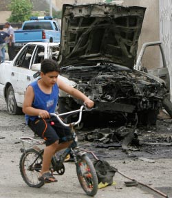 طفل عراقي يلعب أمام سيارة انفجرت في بغداد أمس ( ثائر السوداني - رويترز)