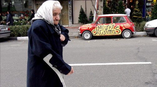 عجوز إيرانيّة تمرّ بالقرب من سيّارة تحمل عبارة «ميلاد مجيد» في طهران الأحد الماضي (أ ب)