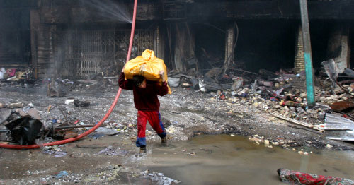 فتى عراقي يركض حاملاً كيس ثياب عند موقع انفجار سوق الشورجة في بغداد أمس (أ ب)