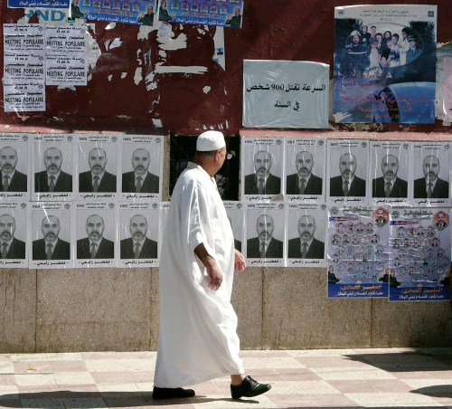 جزائري يمرّ أمام ملصقات لصور مرشّحين للانتخابات في الجزائر أمس (أ ب)