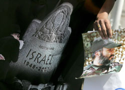 إيراني يحمل شعاراً معادياً لإسرائيل وصورة لعماد مغنيّة في طهران أمس (بهروز مهري ـــ أ ف ب)
