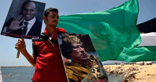 فلسطيني يحمل صورتي الزعيم الليبي وابنه بانتظار وصول سفينة «الأمل» في غزة أمس (خليل حمرا ـ أ ب)