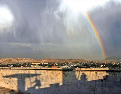 ظلال فتية أفغان تحت خيوط قوس قزح في سماء كابول أمس (أحمد مسعود - رويترز)