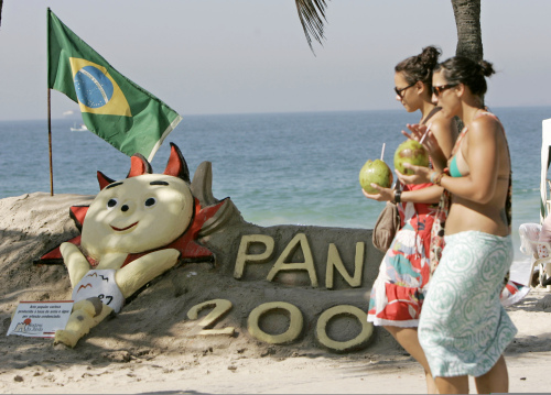 برازيليّتان تمرّان إلى جانب رمز دورة «بان أميركان» الرياضيّة على شاطئ كوباكابانا في ريو دي جانيرو أمس (سيلف