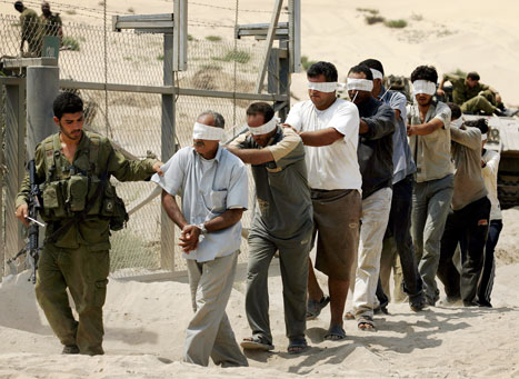 جندي إسرائيلي يقود معتقلين فلسطينيين في غزة أمس (دايفيد فرست - أ ف ب)