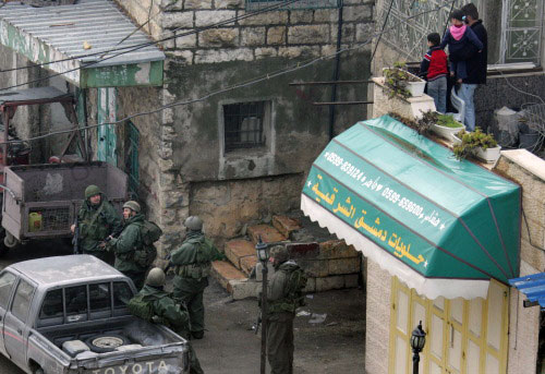 فلسطينيون يراقبون جنوداً إسرائيليين خلال مداهمة في بيت أمّر في الضفة (حازم بدر - أ ف ب)