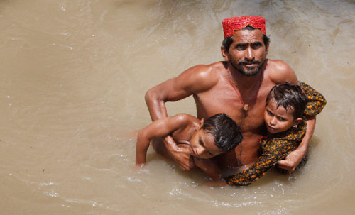 باكستاني يحمل ولديه وسط الفياضانات (أختار سومرو ــ رويترز)