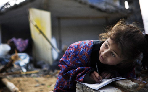طفلة فلسطينية تدرس أمام منزلها المدمر في بيت لاهيا أمس (ماركو لونغاري - أ ف ب)