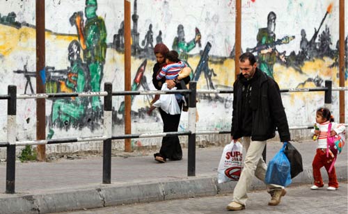 أسرة فلسطينية تمر بالقرب من جدار يحمل رسومات لمقاومين فلسطينيين في غزة أمس (حاتم موسى - أ ب)