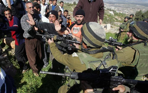 جنود إسرائيليون يشهرون أسلحتهم في اتجاه فلسطينيين بعدما اقتحم مستوطنون قرية صافا في الضفة الغربية أمس (حازم بادر - أ ف ب)
